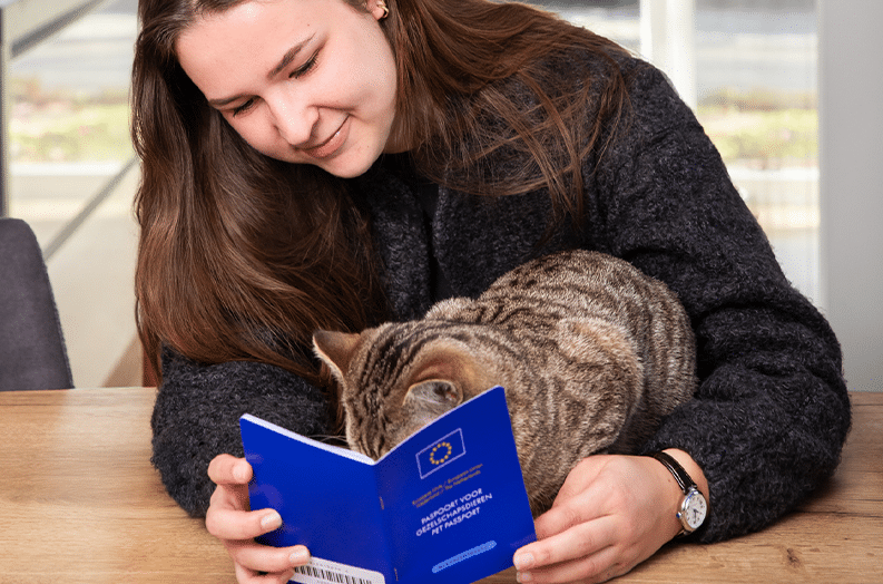 Vrouw toont dierenpaspoort aan kat tijdens controle op tafel